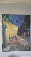 Large framed art print of a night cafe terrace scene on a wall.