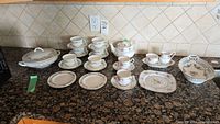 Full view of entire china set including teapot, cups, saucers, plates, creamer, sugar bowl, and serving bowls on granite countertop.
