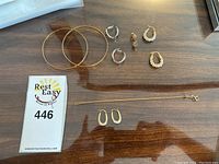 Overhead view of two bangles, chain bracelet and four pairs of earrings on wood surface next to numbered lot card