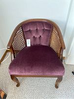 Front angle view of arm chair showing purple tufted velvet backrest, seat cushion, wooden frame, and cane sides.