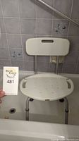 Front view of white shower chair seated in bathtub with hand grips on seat and solid backrest with a built-in handle.