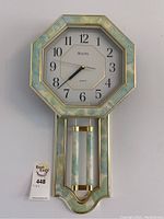 Front view of the Bulova wall clock showing the clock face and decorative pendulum under glass with a marbleized pastel green and cream frame.