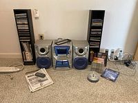 Wide front view showing Panasonic stereo system, speakers, two tall CD racks, cordless phones and media discs on floor