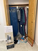 Clothing rack with hanging garments and garment bags, plus sewing and miscellaneous items on the floor.
