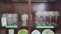 Shelved vintage cut crystal glasses including tall highball, small cordial, and multiple stemmed wines or cocktail glasses with detailed cuts