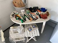 Another angled photo of the white oval plastic garden table and surrounding items showing various garden tools and white folding chairs.