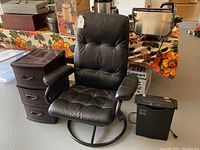 Full view of black leather swivel chair, plastic storage drawers, and black paper shredder on floor near floral tablecloth-covered table.