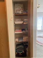 Closet shelf with multiple folded linens including sheets, towels, throws, and blankets