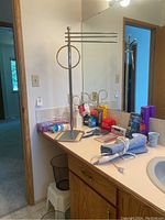 Photo of MCM towel rack with three horizontal rods and circular ring on bathroom counter with various packed toiletries and devices.