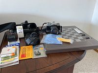 Minolta XG-1 camera with accessories on table including manuals, cleaning cloth, and case