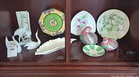 Shelf displaying porcelain decorative plates, bird figurines, and plate hangers
