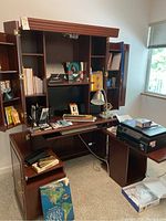 Office desk loaded with various office items including books, files, lamp, and printer on side table