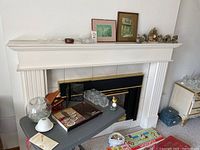 Wide view showing mantle with framed prints, crystal pieces, and figurines on top and table with music box and coasters