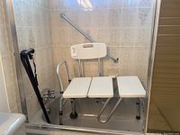 White plastic shower chair with metal frame and three-section perforated seat positioned in bathtub, with two black canes leaning on the tub wall.