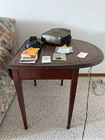 Front angle of wooden side table with two extended half-oval leaves, showing wear marks and items placed on top.