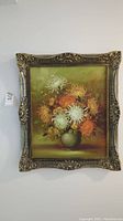 Full view of the original oil painting in ornate gold frame showing bouquet of chrysanthemums in a green vase on muted warm background.