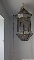 Side angle view of the hanging swag lamp showing the hexagonal prism shape with smoked glass panels and brass frame, suspended by metal chain.