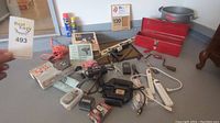Overview of multiple tools and electrical accessories including power drill, sander, extension cords, power strip, manual hand saw, and other items.