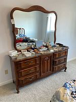 Full view of the dresser with mirror showing carved decorative elements and multiple drawers, surface with various small items