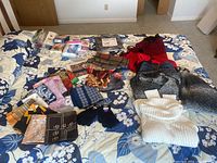 Overhead photo showing a collection of women's scarves, sweaters, socks, gloves, and accessories spread out on a floral bedspread.