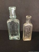 Two antique medicine bottles, larger clear rectangular 'Nerviline' bottle and smaller narrow 'Dr. Bell's Medical Wonder' bottle, both with embossed lettering.
