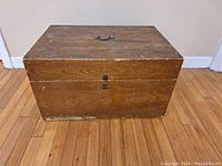 Full view of the rectangular wooden box showing its top, front, and side faces, wooden construction with visible scratches and paint marks.