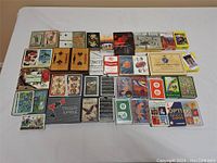 Wide photo showing about 40 assorted playing card decks arranged on a flat surface, various brands and designs visible.