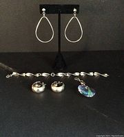 Photo showing two pairs of earrings on black stand, sterling silver bracelet laid flat, and crystal heart pendant beside them, all on black surface.