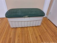 Full view of the large rectangular Rubbermaid storage tote with white base and green lid placed on wooden floor.