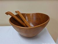 Side angle showing large wooden salad bowl with two wooden servers inside, highlighting the wood grain and bowl shape.