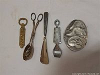 Photo showing five items: brass bottle opener, metal salad tongues, metal shoehorn, and decorative coin dish with animal motif.
