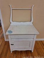 Front view of the white painted wash stand with harp showing top and cabinet door with latch, with visible paint chipping