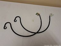 Two black metal arch-shaped plant hanger brackets laid on a white surface, showing their curved hook ends and metal construction.