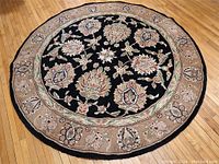 Full view of round rug with black and beige floral design on hardwood floor.