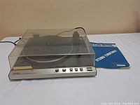 Front angled view of Toshiba SR-F200 stereo turntable with dust cover closed and manual beside it.