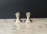 Pair of silver candle holders on marble surface with black background showing overall size and condition