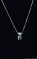 Front view of sterling silver necklace with aquamarine and crystal pendant against black background.