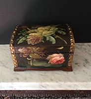 Front view of the hand painted tole wooden chest with floral design and metal clasp.