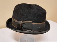 Side view of the black felt fedora hat with brown grosgrain ribbon and bow, showing slight wear on felt and clear details of ribbon and hat shape.