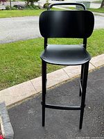 Photo of single black bar stool showing front angle, rounded backrest and seat, metal legs and footrest.