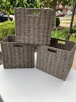 Three gray woven rectangular baskets stacked outside on a white table, showing shape and size