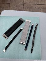 Five bracelets arranged on a table showing variety of material and widths.