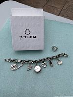 Charm bracelet laid out flat with box in background, showing six charms and watch charm in center