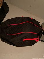 Quilted black carry storage bag with red accents closed and placed on floor