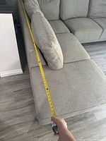 Measuring chaise length from inner corner to front end with yellow tape measure reading approximately 76 inches