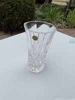 Clear crystal vase with a gold label sticker visible on the front, showing its design and shape.