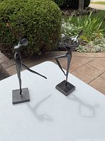 Two modern streamline metal dancer figurines on square bases, one with leg extended forward, the other with bent leg and arm curved over head.
