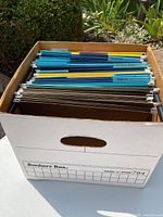 Top view of box filled with greenish-blue and beige hanging file folders, some with visible labels