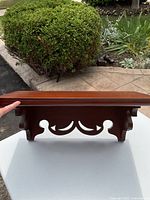 Wooden floating shelf held by hand showing Victorian carved design underneath and smooth top surface.