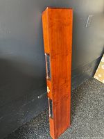 Solid wood rectangular floating shelf standing upright, showing its thickness and two metal bracket components on the back for wall mounting.